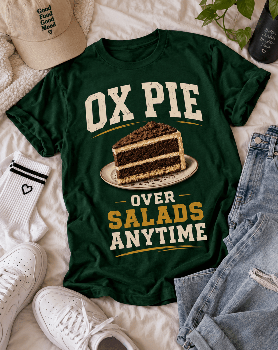 Flatlay of a green Ox Pie Over Salads Anytime t-shirt with cake, jeans and sneakers